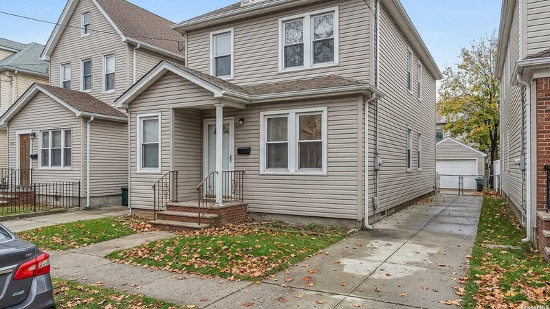 A detached two-family frame house with a small front porch and driveway in Glendale, Queens